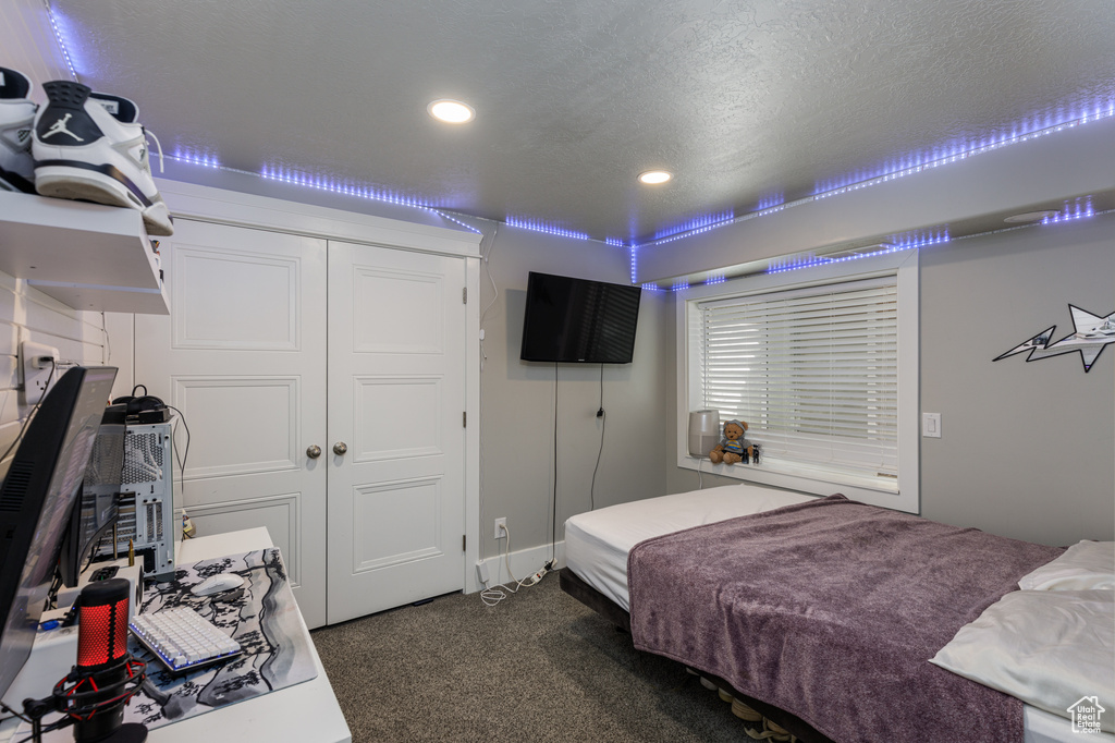 Bedroom featuring a textured ceiling, dark colored carpet, and a closet