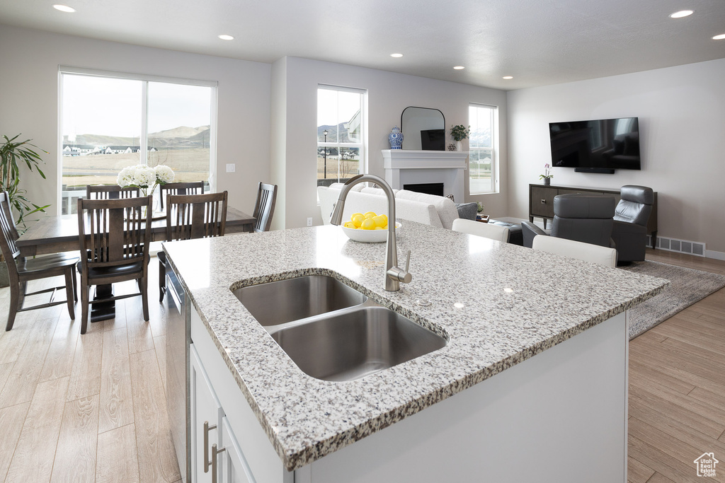 Kitchen with white cabinets, light stone countertops, light hardwood / wood-style floors, and an island with sink