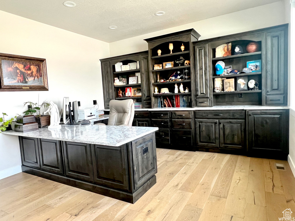 Bar featuring built in desk, light stone countertops, and light hardwood / wood-style floors