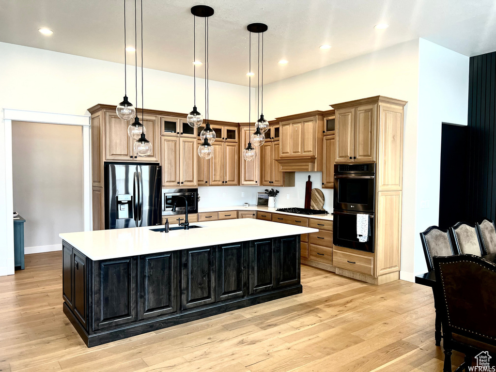 Kitchen featuring a kitchen island with sink, sink, hanging light fixtures, black appliances, and light hardwood / wood-style flooring