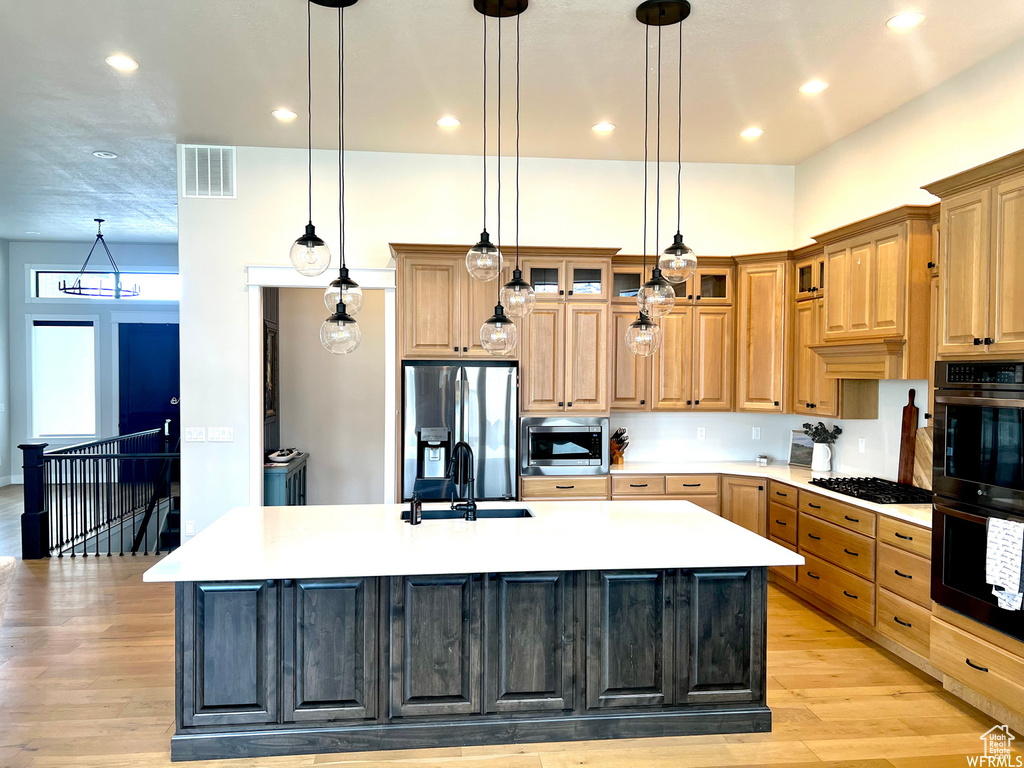 Kitchen with black appliances, an island with sink, pendant lighting, and light hardwood / wood-style floors