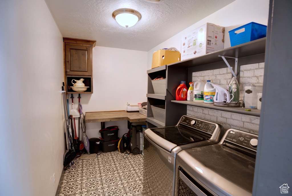 Laundry room featuring a textured ceiling, light tile floors, and washing machine and clothes dryer