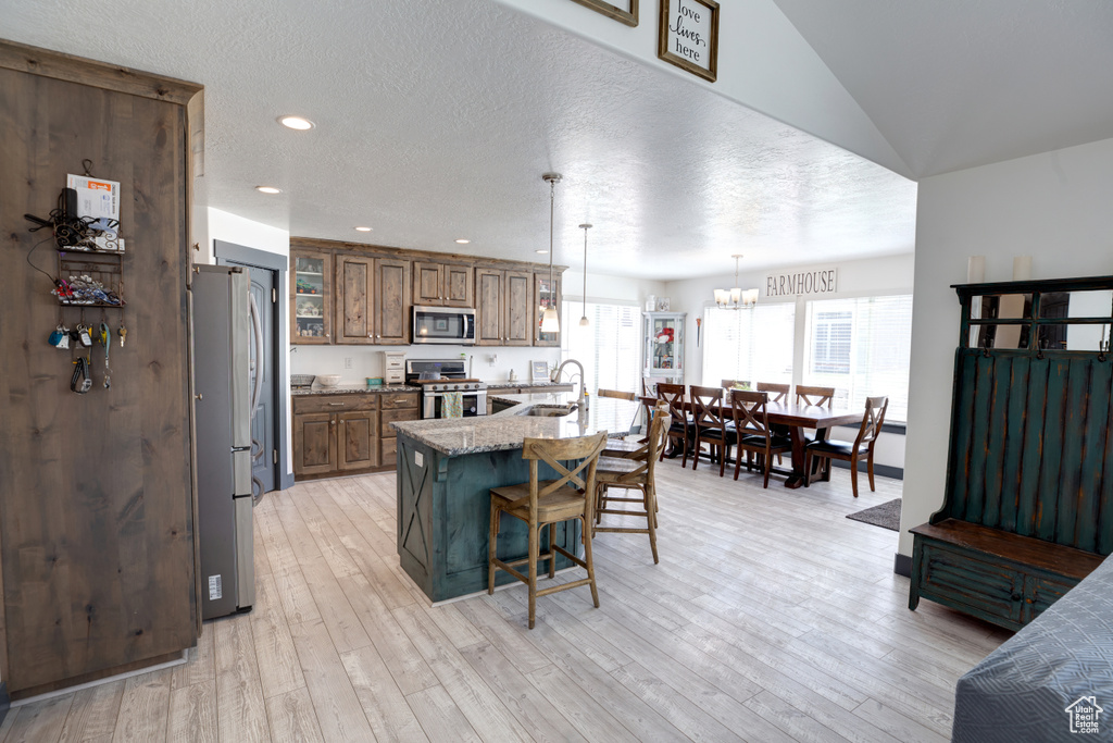 Kitchen featuring light stone countertops, stainless steel appliances, light hardwood / wood-style floors, a kitchen breakfast bar, and pendant lighting