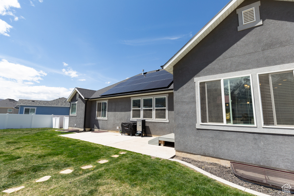 Rear view of property with solar panels, a patio, and a lawn