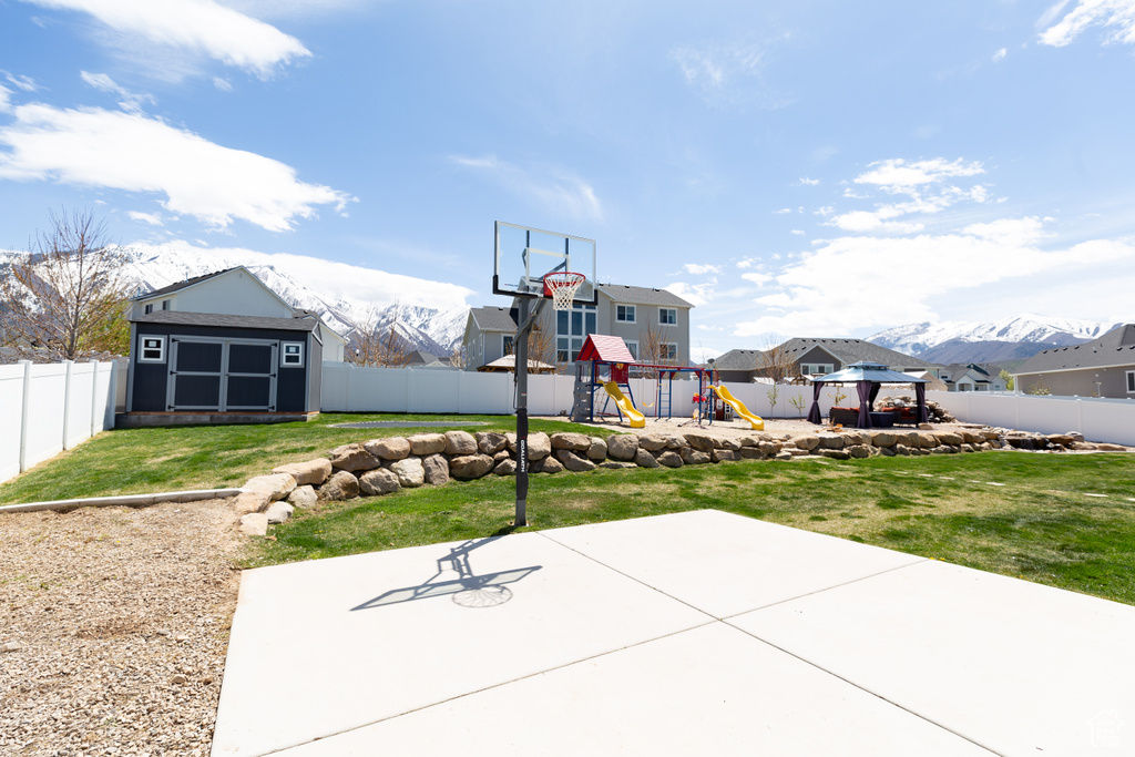 View of basketball court featuring a playground, a gazebo, a mountain view, and a lawn