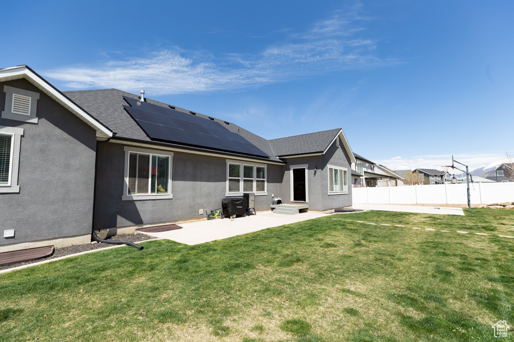 Back of house with solar panels, a yard, and a patio