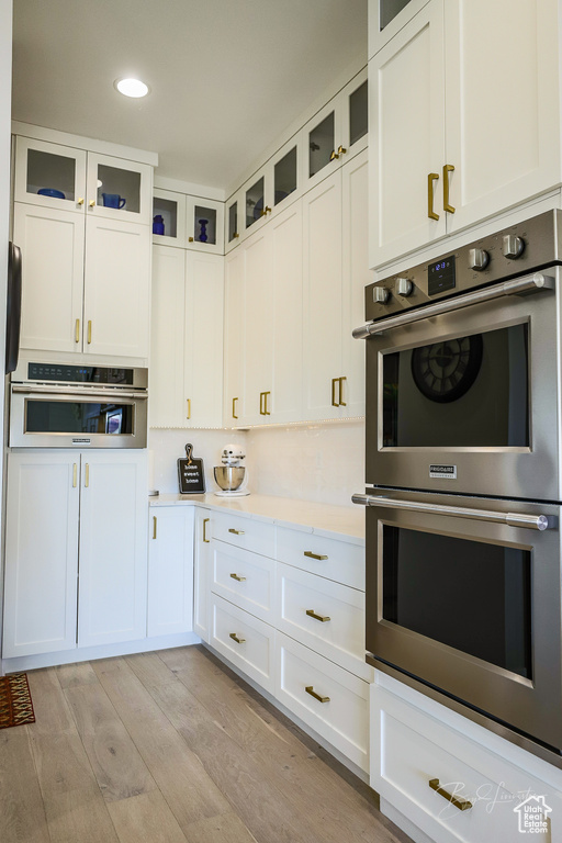 Kitchen featuring white cabinets, double oven, and light hardwood / wood-style flooring