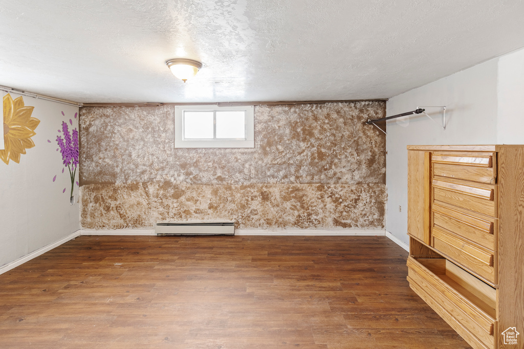 Basement featuring a textured ceiling, dark wood-type flooring, and a baseboard heating unit