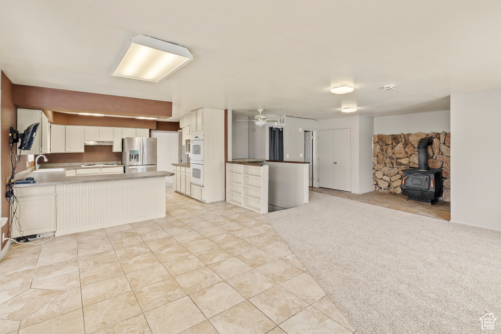 Kitchen with ceiling fan, a wood stove, sink, stainless steel refrigerator with ice dispenser, and light colored carpet