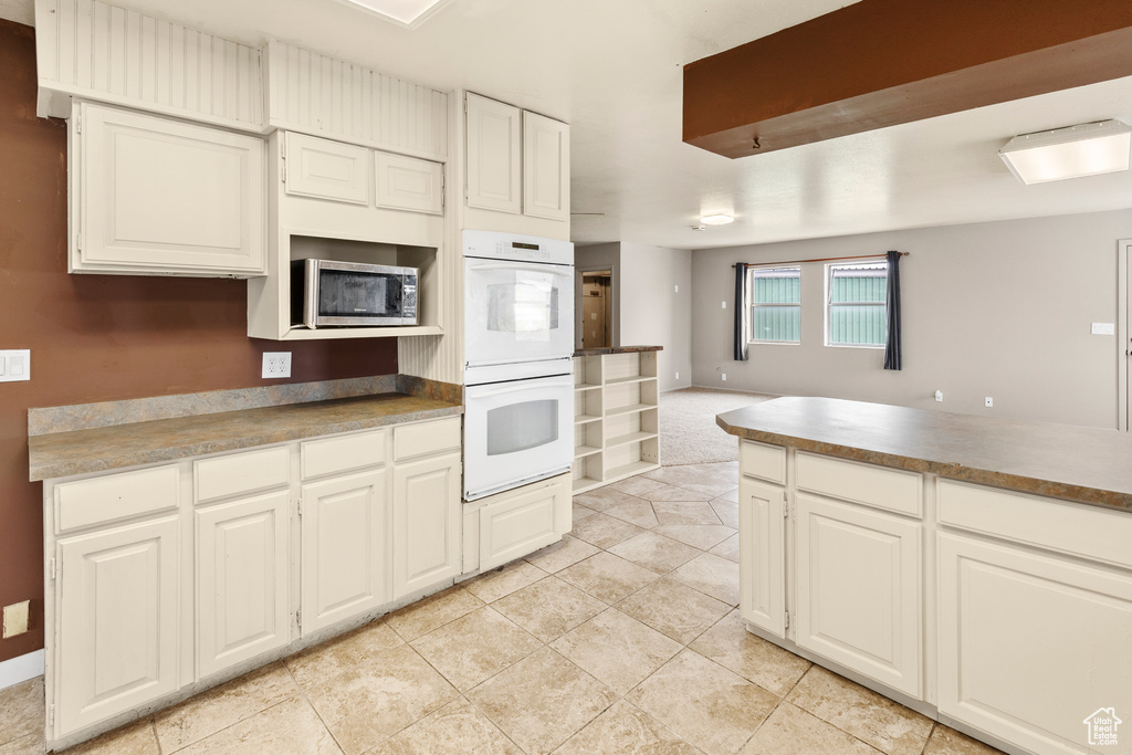 Kitchen with white double oven, light tile floors, and white cabinetry