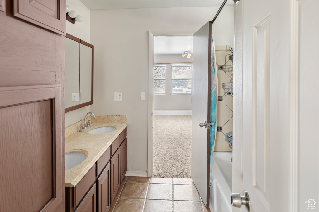 Bathroom with tile floors, vanity with extensive cabinet space, double sink, and washtub / shower combination
