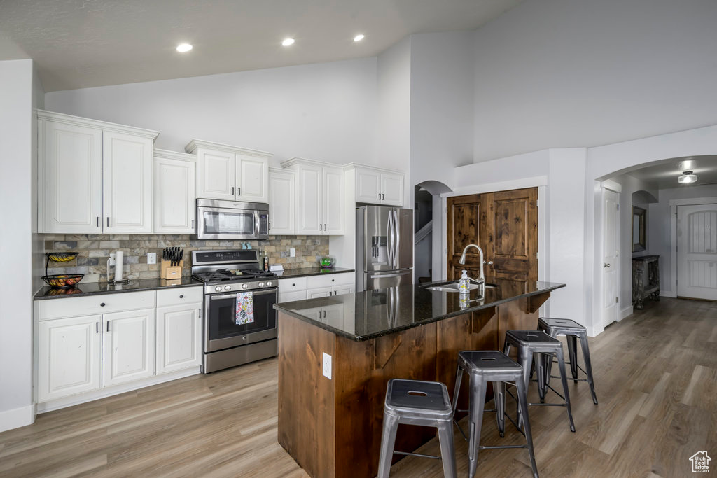 Kitchen featuring appliances with stainless steel finishes, light hardwood / wood-style floors, a kitchen breakfast bar, sink, and a center island with sink