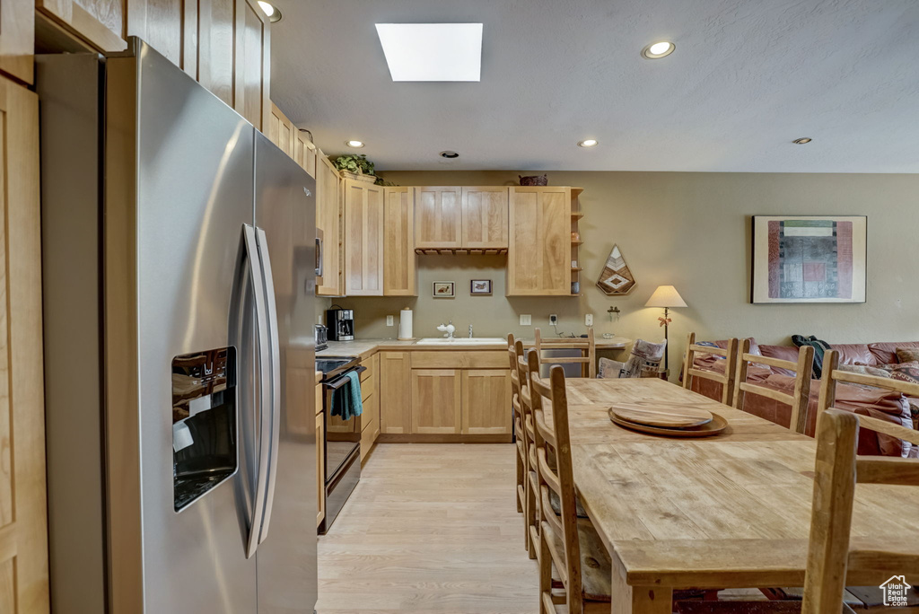 Kitchen featuring stainless steel fridge, range with electric cooktop, a skylight, light hardwood / wood-style flooring, and light brown cabinets
