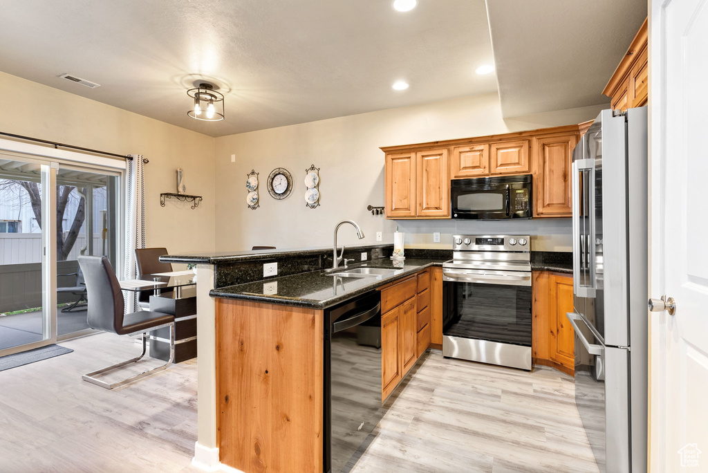 Kitchen featuring light hardwood / wood-style flooring, kitchen peninsula, dark stone countertops, and black appliances
