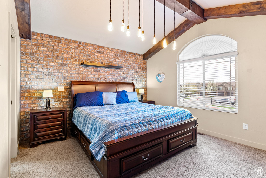 Carpeted bedroom with lofted ceiling with beams and brick wall