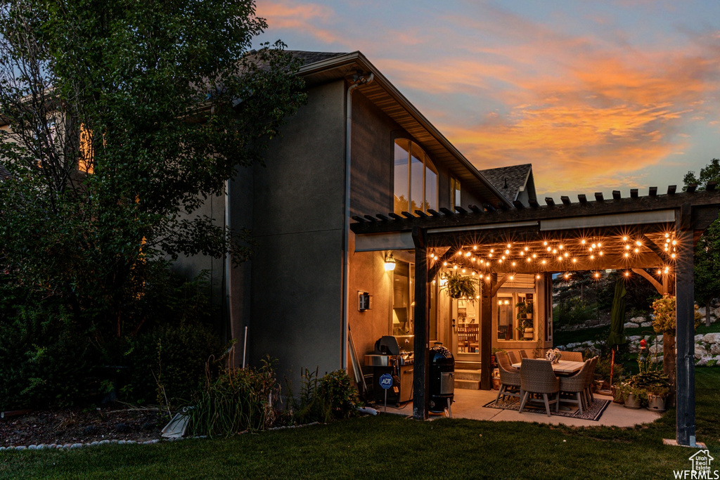 Back house at dusk featuring a pergola, a lawn, and a patio