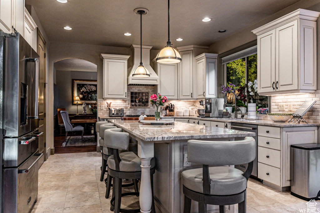 Kitchen featuring pendant lighting, tasteful backsplash, a kitchen island, light stone counters, and stainless steel appliances