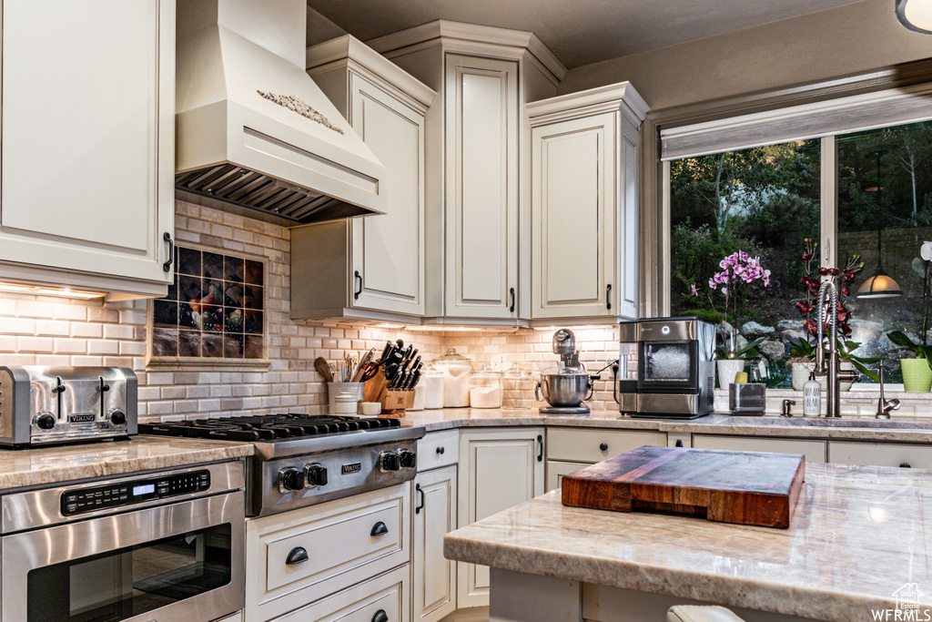 Kitchen featuring backsplash, premium range hood, light stone countertops, and stainless steel appliances