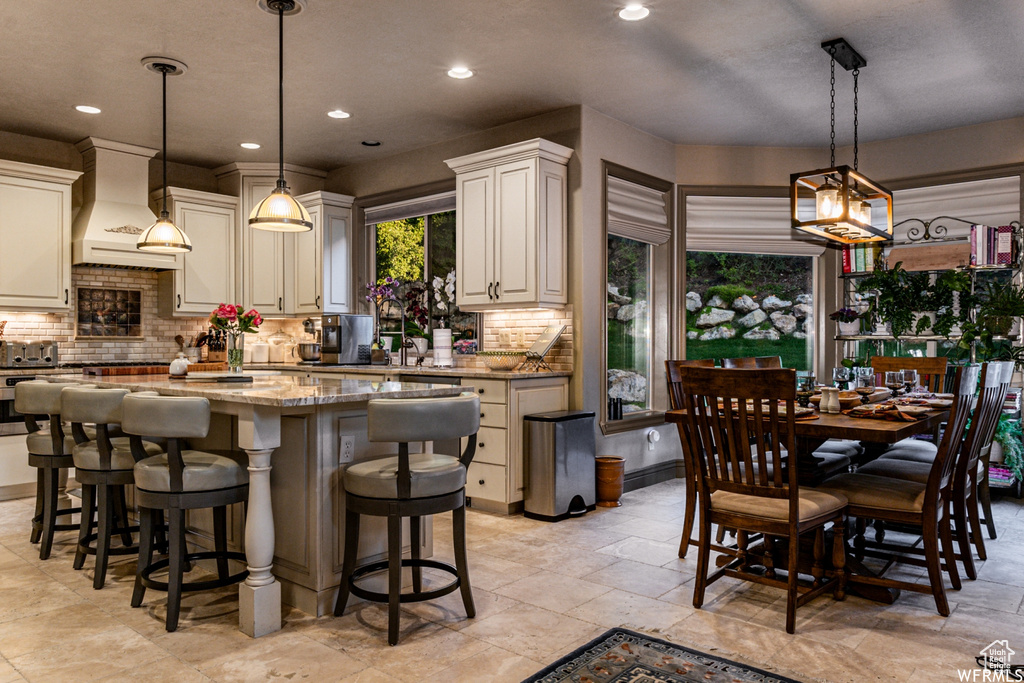 Kitchen with light tile floors, custom range hood, light stone countertops, and pendant lighting