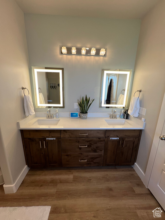 Bathroom featuring dual sinks, vanity with extensive cabinet space, and wood-type flooring