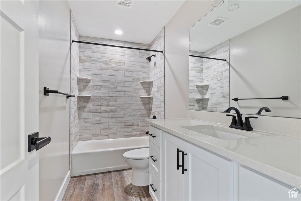 Full bathroom featuring tiled shower / bath combo, toilet, vanity, and hardwood / wood-style flooring