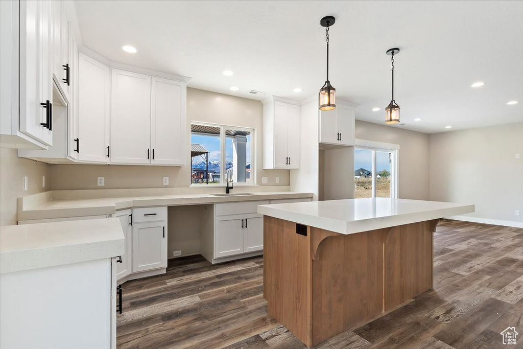 Kitchen featuring a breakfast bar area, white cabinets, a center island, dark hardwood / wood-style flooring, and pendant lighting