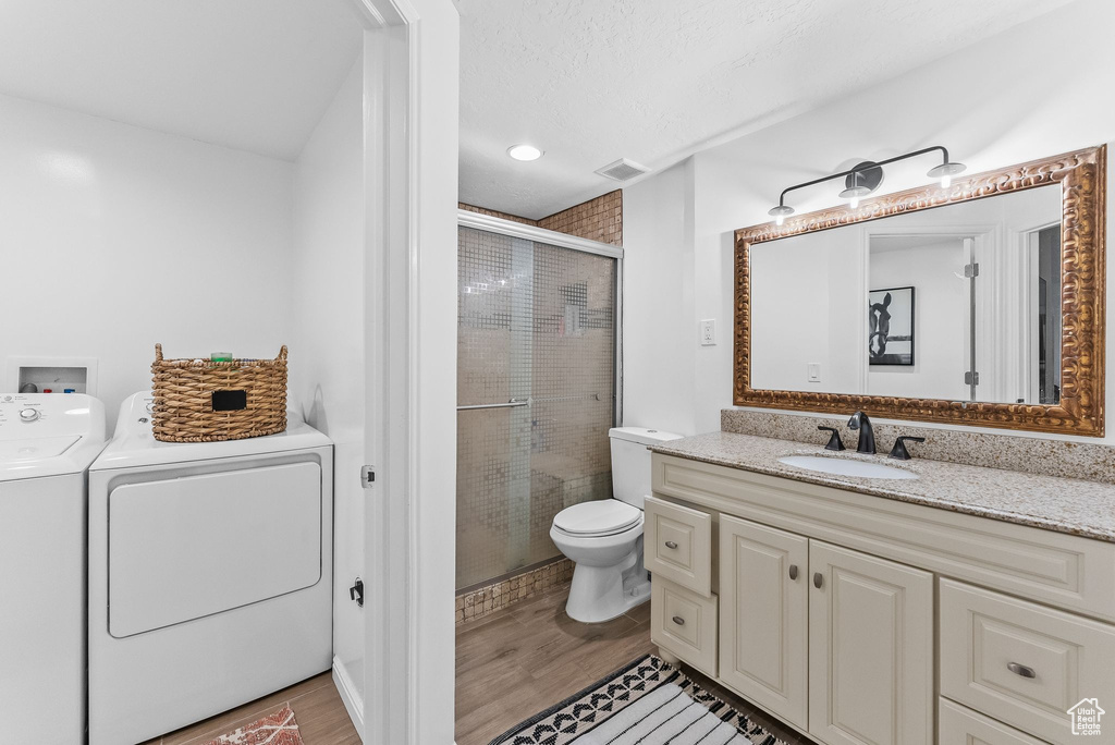 Bathroom featuring toilet, an enclosed shower, washer and dryer, large vanity, and hardwood / wood-style flooring