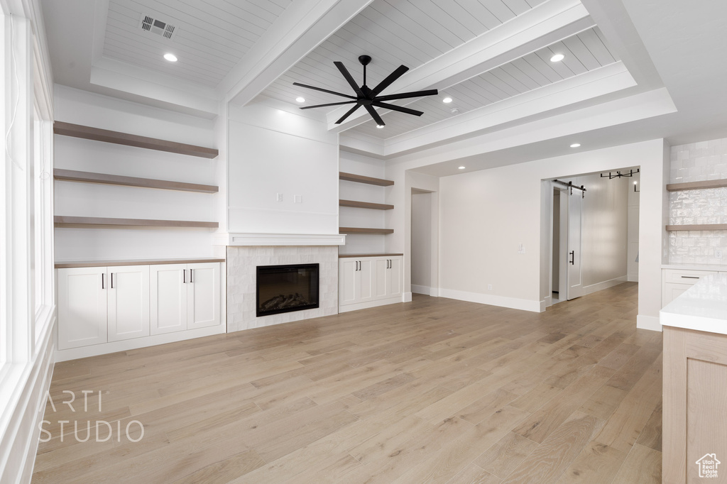Unfurnished living room with beam ceiling, light wood-type flooring, a barn door, and a fireplace