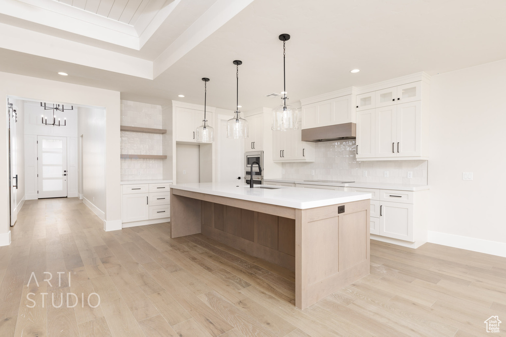 Kitchen featuring pendant lighting, a center island with sink, light wood-type flooring, and white cabinetry