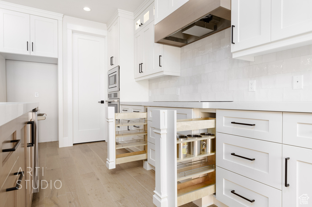 Kitchen with premium range hood, white cabinetry, stainless steel microwave, tasteful backsplash, and light hardwood / wood-style floors