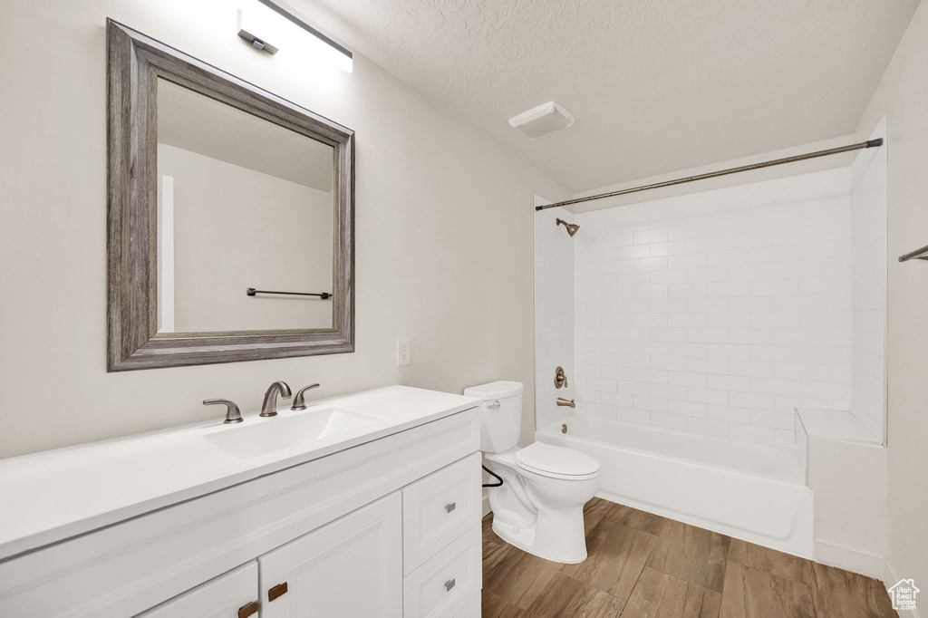 Full bathroom with toilet, hardwood / wood-style flooring, a textured ceiling, vanity, and tiled shower / bath