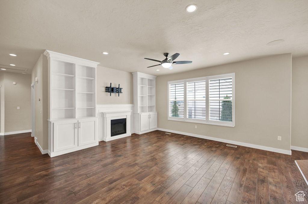 Unfurnished living room featuring dark hardwood / wood-style flooring, ceiling fan, a textured ceiling, and built in shelves