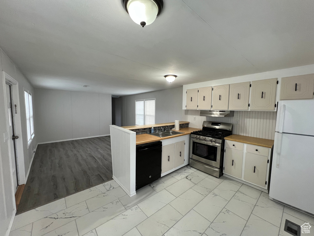 Kitchen with stainless steel gas stove, dishwasher, white refrigerator, and light tile flooring