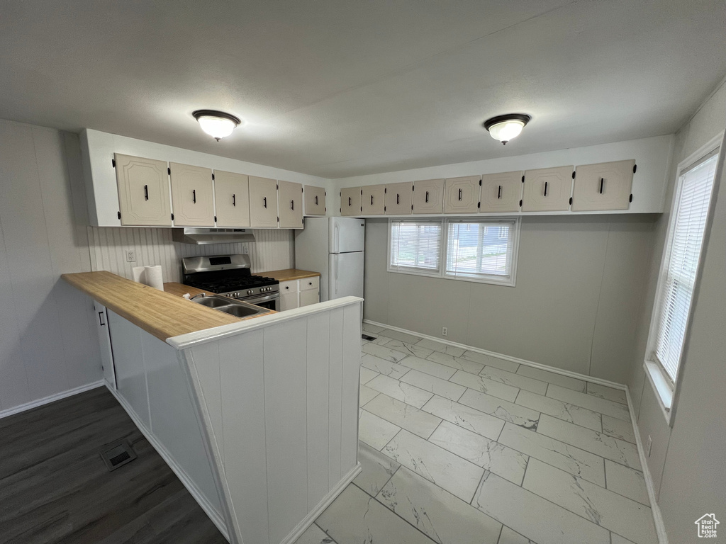 Kitchen with light tile floors, white refrigerator, kitchen peninsula, gas stove, and sink