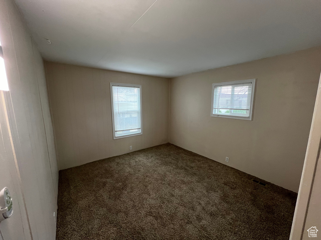 Unfurnished room featuring dark carpet and a healthy amount of sunlight
