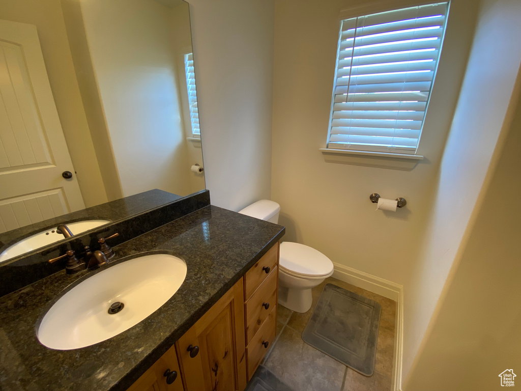 Bathroom with a wealth of natural light, toilet, vanity with extensive cabinet space, and tile flooring
