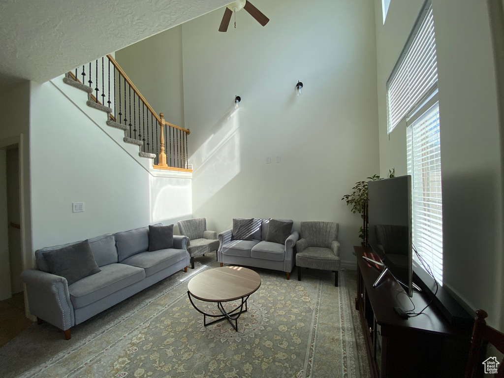 Living room with ceiling fan, a textured ceiling, and a high ceiling