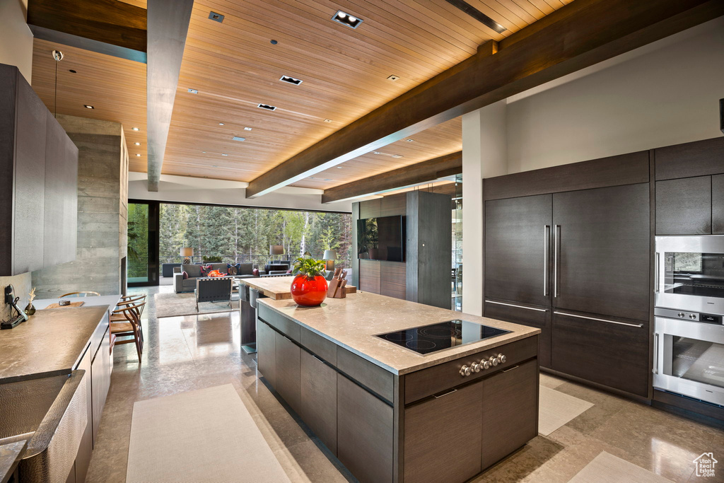 Kitchen featuring appliances with stainless steel finishes, beam ceiling, wood ceiling, dark brown cabinetry, and a kitchen island