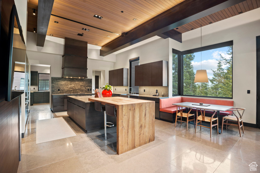 Kitchen with beamed ceiling, a center island, backsplash, dark brown cabinets, and custom range hood