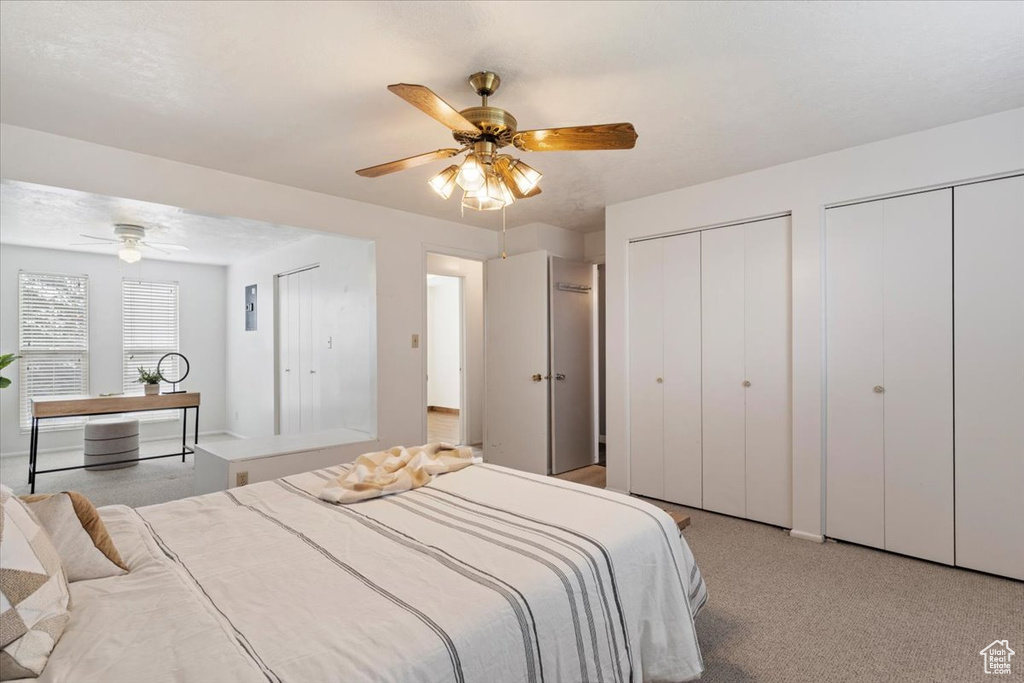 Bedroom with light carpet, ceiling fan, and two closets