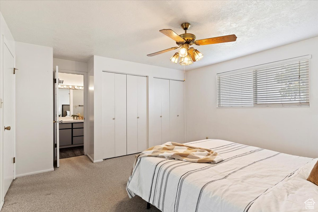 Carpeted bedroom featuring ceiling fan, two closets, and connected bathroom
