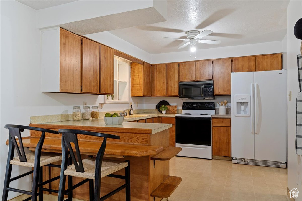 Kitchen featuring a kitchen bar, ceiling fan, white appliances, sink, and light tile flooring