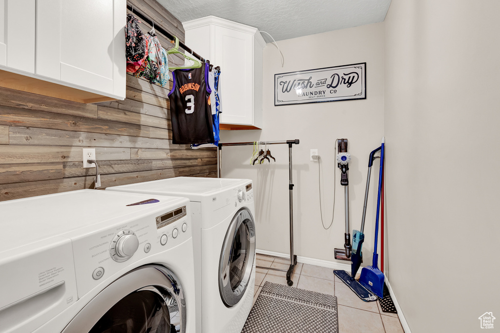 Clothes washing area featuring wood walls, light tile floors, a textured ceiling, cabinets, and independent washer and dryer