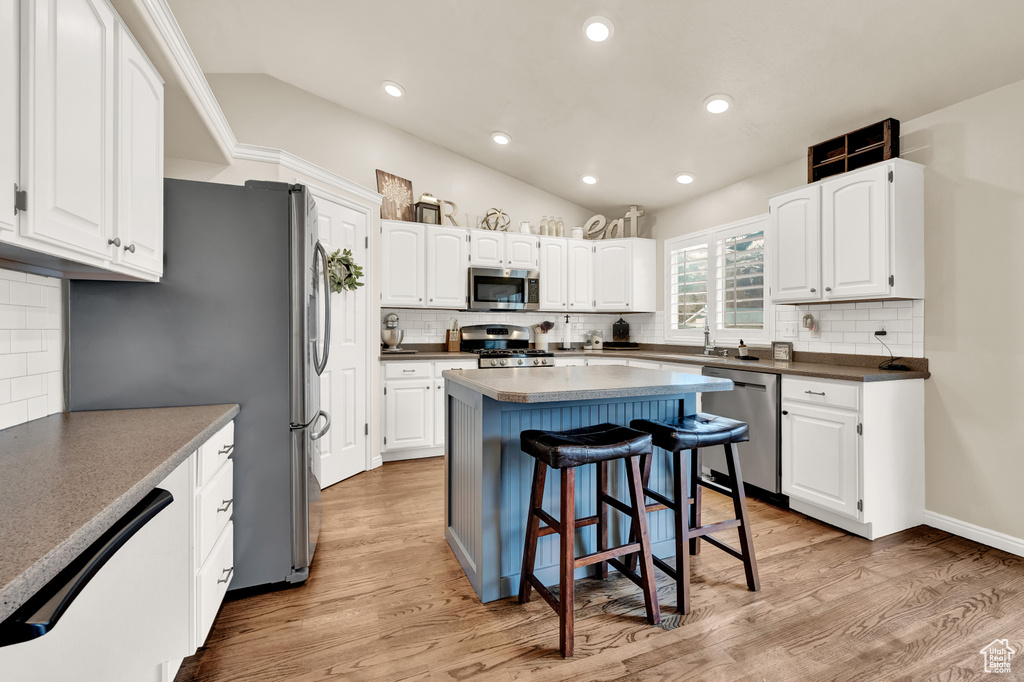 Kitchen with white cabinets, appliances with stainless steel finishes, a breakfast bar, tasteful backsplash, and light wood-type flooring