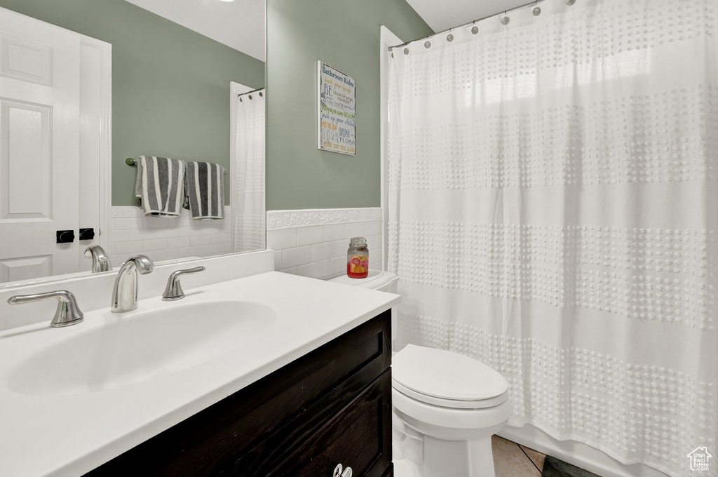 Bathroom featuring tile walls, tile floors, toilet, and vanity