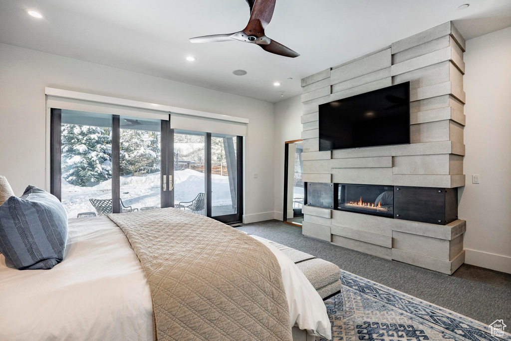Bedroom featuring ceiling fan, a large fireplace, access to exterior, and dark colored carpet