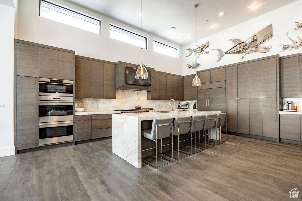 Kitchen featuring dark wood-type flooring, stainless steel appliances, tasteful backsplash, and a breakfast bar