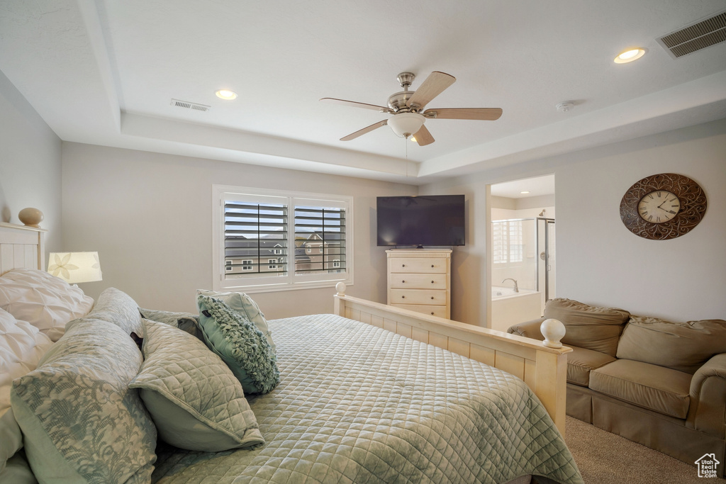 Bedroom with carpet flooring, ensuite bath, ceiling fan, and a raised ceiling