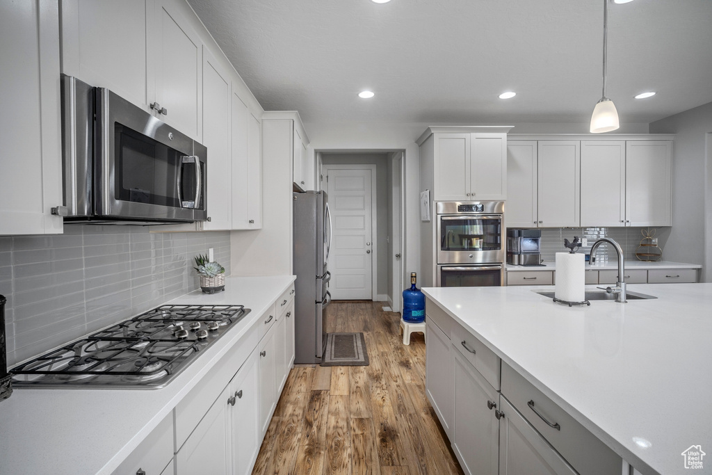 Kitchen featuring white cabinets, appliances with stainless steel finishes, tasteful backsplash, and light wood-type flooring