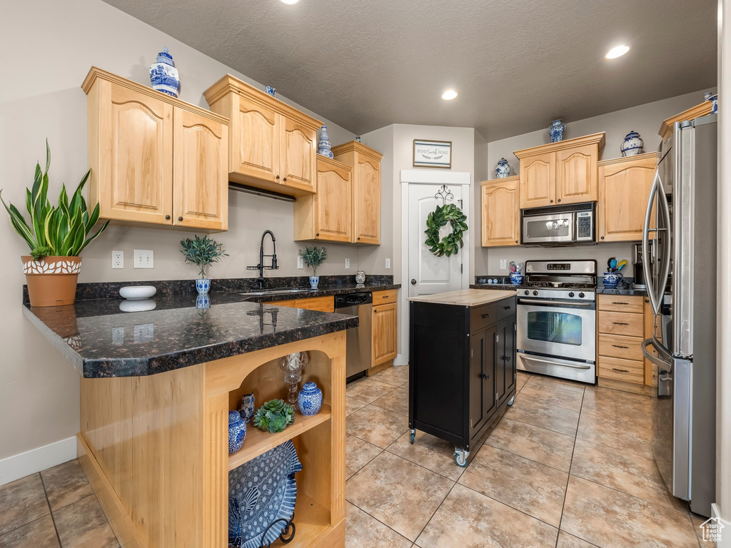 Kitchen featuring appliances with stainless steel finishes, light tile flooring, dark stone countertops, light brown cabinets, and sink